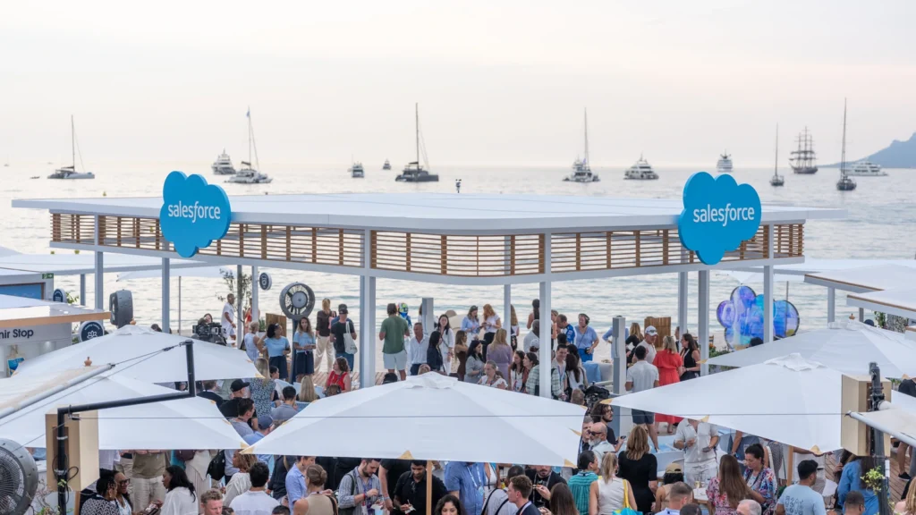 Sunset overhead view of the Sparks-designed Salesforce Beach activation with dual Salesforce cloud logos, packed crowd and yachts on the Mediterranean at Cannes Lions 2026.