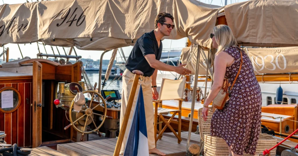 Sparks-cast host welcoming a VIP guest at the O'Remington gangway beside the ship's wheel and French flag at the Sparks-produced Riviera at Dawn breakfast cruise for The Wall Street Journal at Cannes Lions 2026.