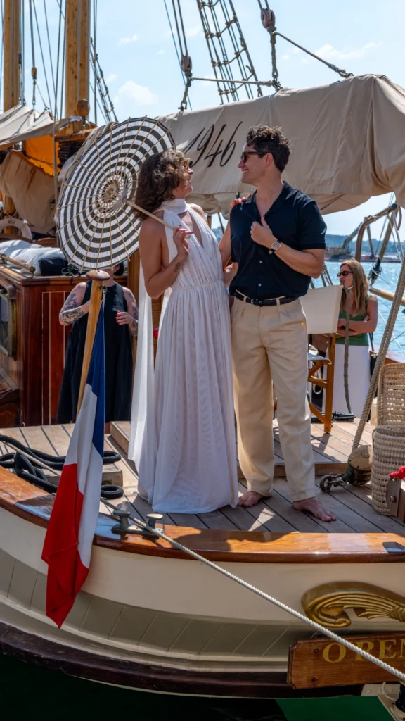 Signature portrait of the two Sparks-cast hosts in 1920s Riviera attire on the bow of the O'Remington with a striped parasol, French flag, and the ship's O'Remington nameplate at the Sparks-produced Riviera at Dawn for The Wall Street Journal at Cannes Lions 2026.