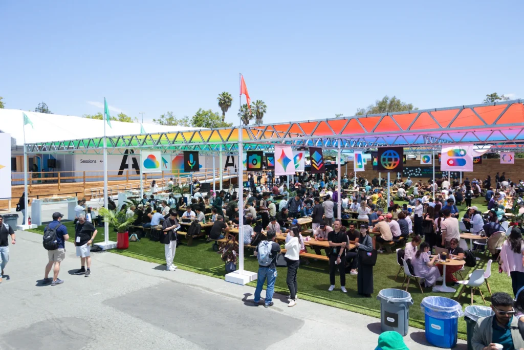 Developers crowd picnic tables under colorful truss canopies at the heart of the campus