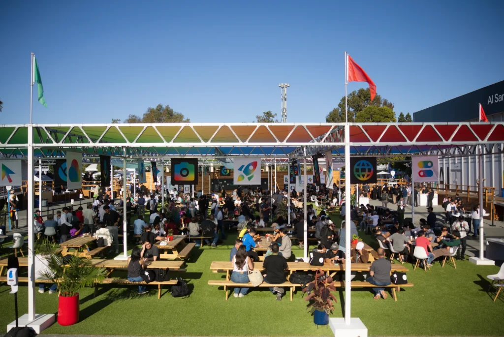 Attendees fill picnic tables across the turf dining lawn under colorful canopies