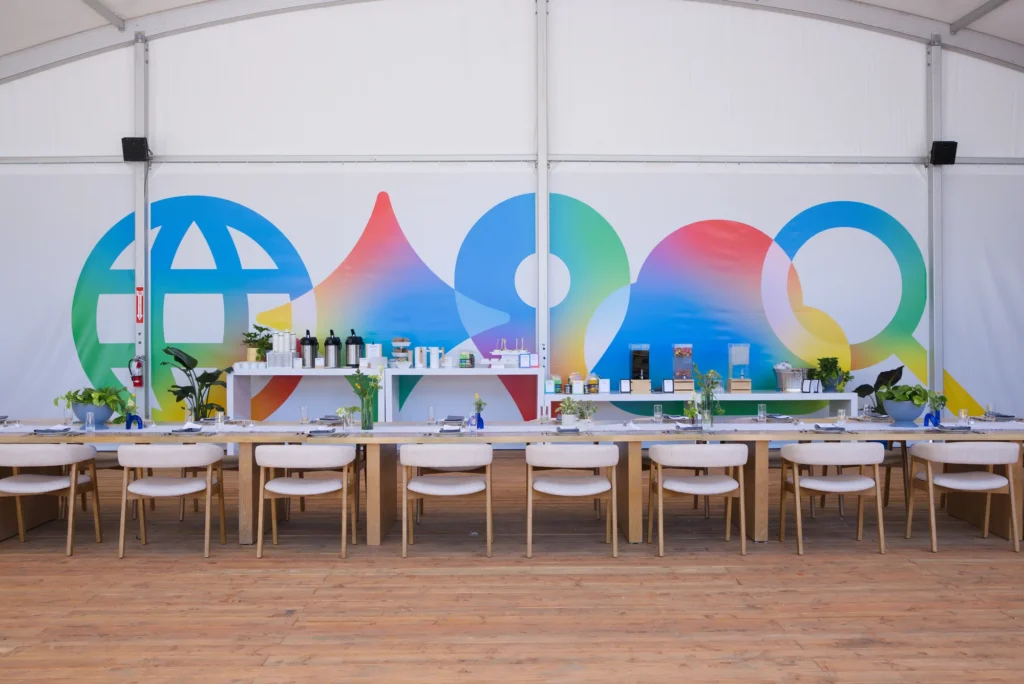 Long dining tables set in front of a colorful Google I/O graphic mural