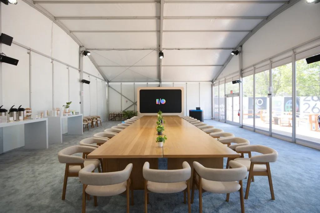 Long wooden conference table with upholstered chairs in a daylit temporary meeting room