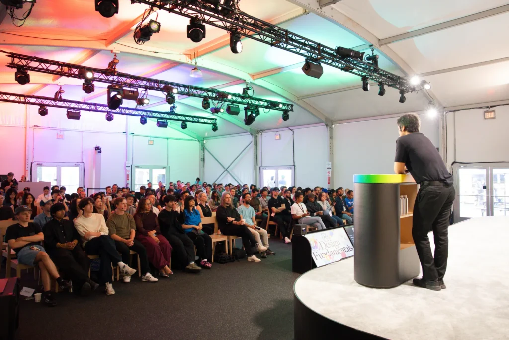 Speaker presents from a round stage to a full tented session room