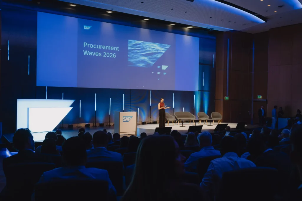 Speaker on the main stage as SAP's Procurement Waves 2026 program opens before a seated audience.