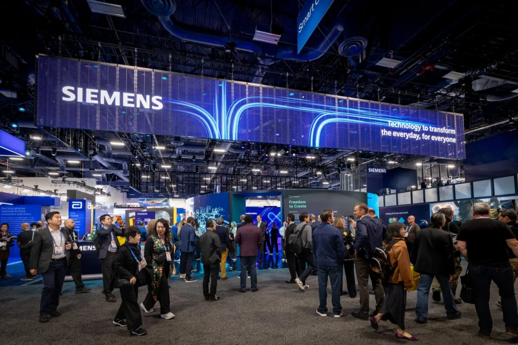 CES 2026 attendees walking beneath the Siemens LED banner toward the exhibit's customer story zones.