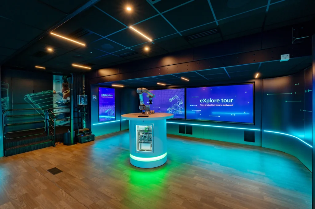 Interior of the Siemens eXplore Tour mobile experience with a robotic arm demo station and LED screens.