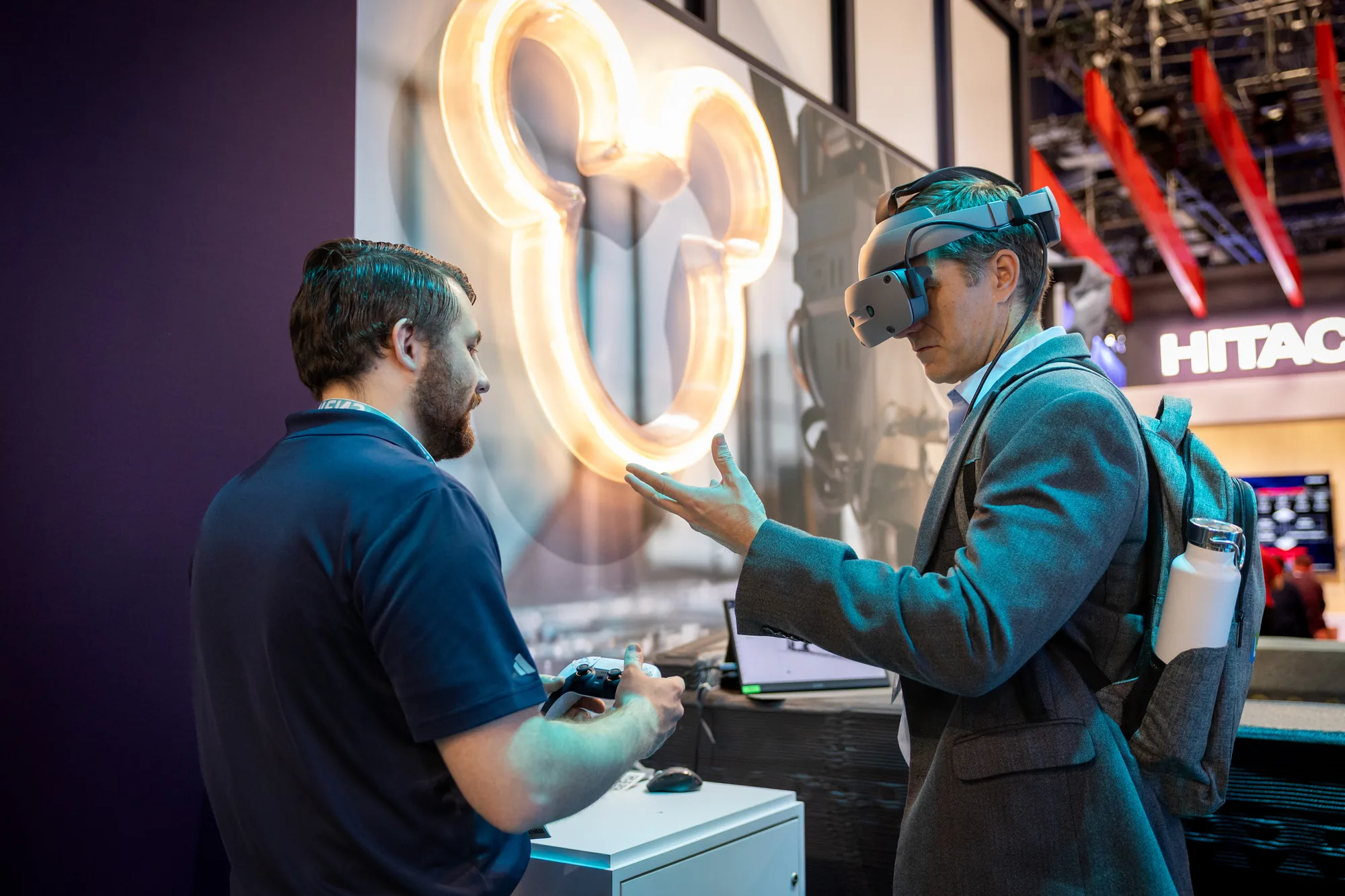 Attendee in a VR headset guided by a presenter beneath a neon Mickey Mouse sign in the Haddy customer zone at Siemens CES 2026.