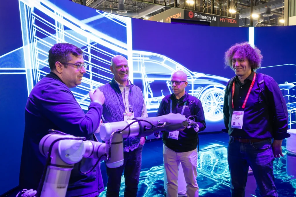 Siemens expert guiding visitors through a hands-on robotic arm demonstration in front of an LED digital wireframe at CES 2026.