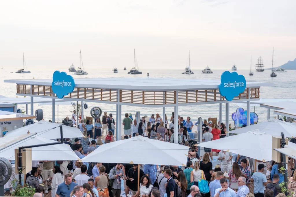 Guests network at Salesforce's beachfront pavilion at Cannes Lions 2026, with yachts on the Mediterranean at dusk behind it.