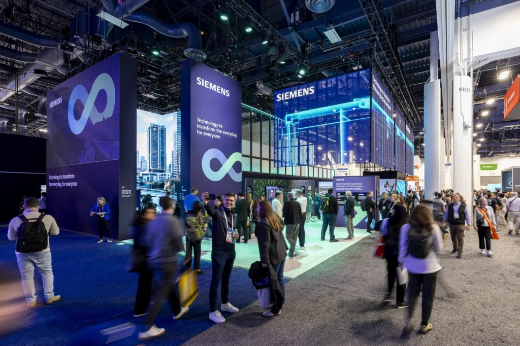 Attendees explore Sparks' Siemens exhibit at CES 2025, with tall navy towers displaying the Siemens Xcelerator logo.