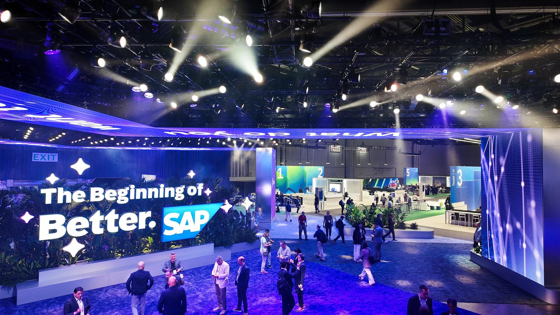 Attendees gather by The Beginning of Better sign under bright lights at the entry