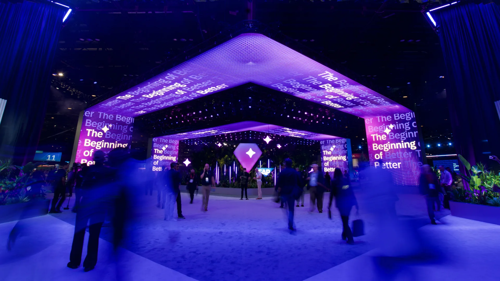 Motion-blurred attendees stream beneath the entrance LED canopy displaying The Beginning of Better
