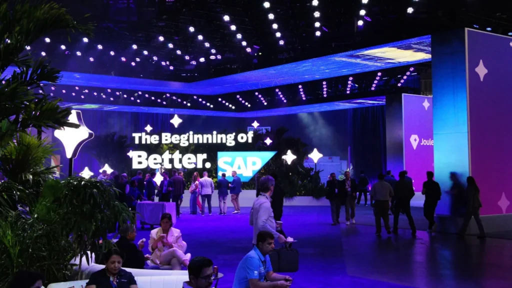 Attendees relax in a planted lounge facing The Beginning of Better entrance sign
