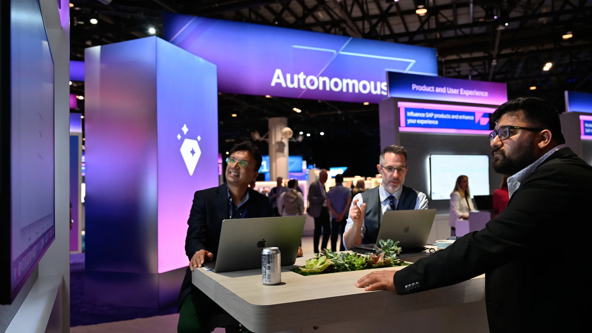 Three attendees gather around laptops at an SAP experience hub demo table