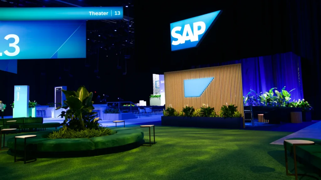 Turf-covered lounge with plants and low tables beside Theater 13 and an SAP sign