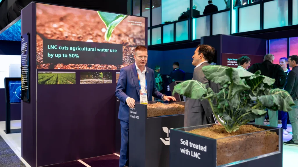 Two men talk beside a plant in a planter labeled Soil treated with LNC