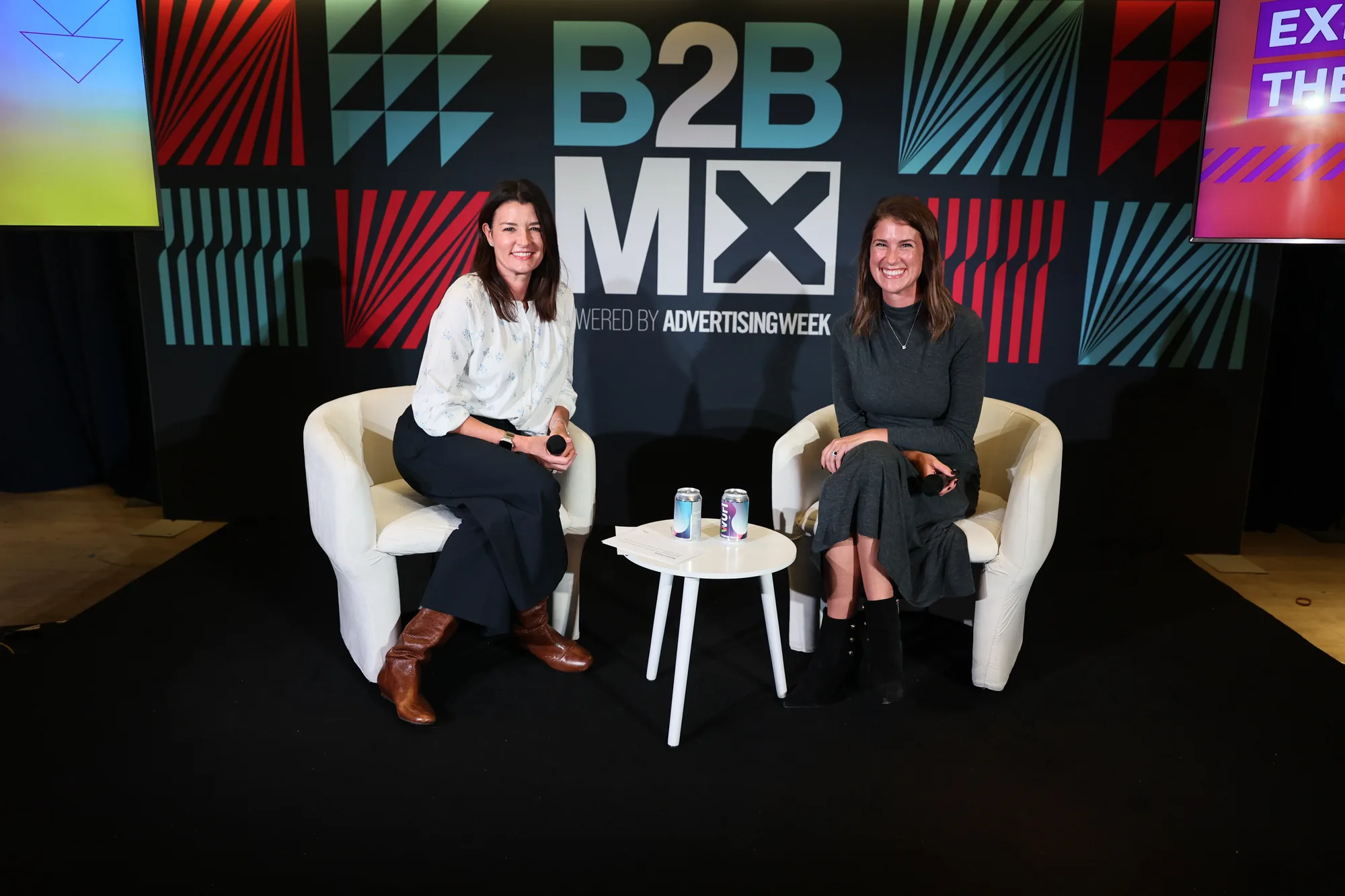 Melissa Levy and Madeline Schofield pose smiling in white armchairs on the B2BMX stage
