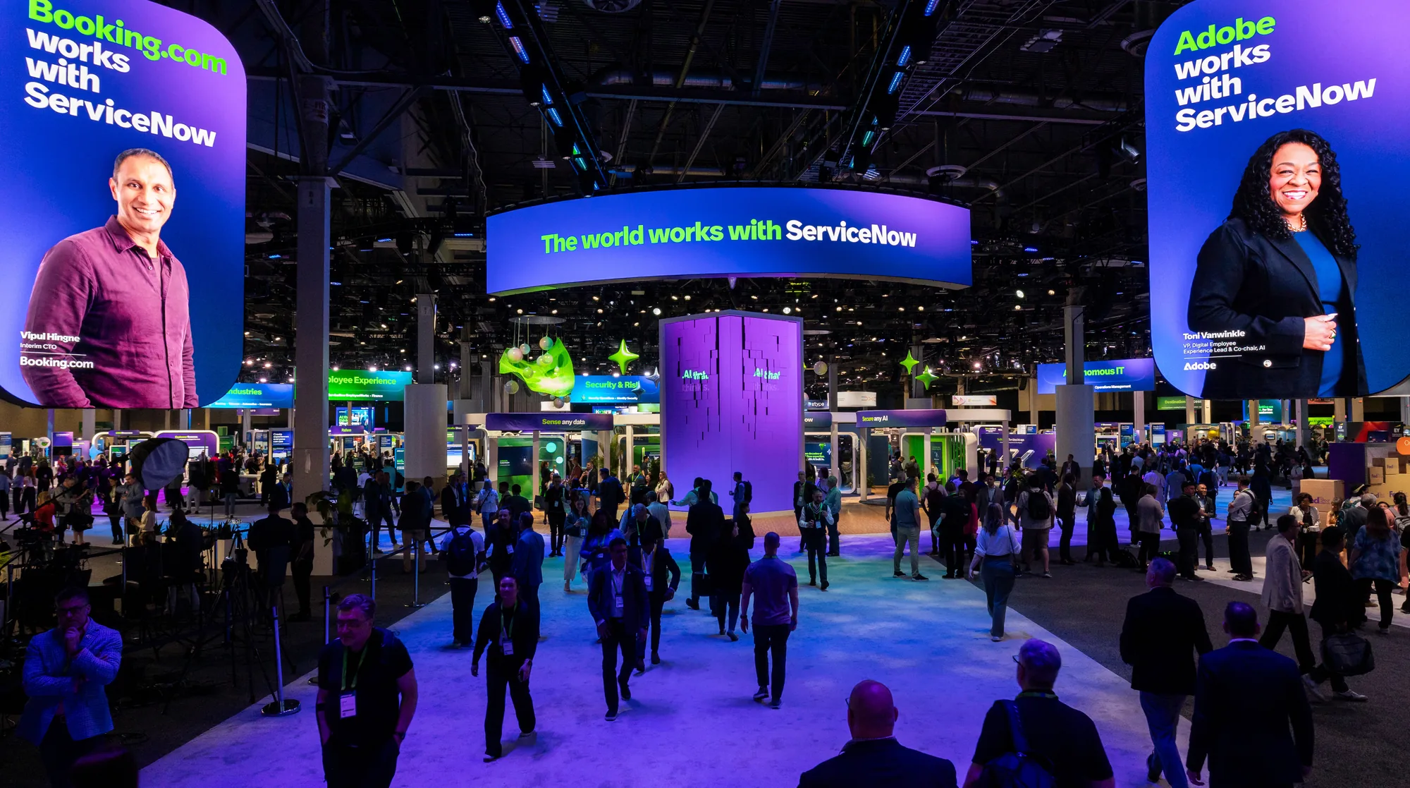 Attendees walk the ServiceNow show floor beneath curved LED screens reading "The world works with ServiceNow."