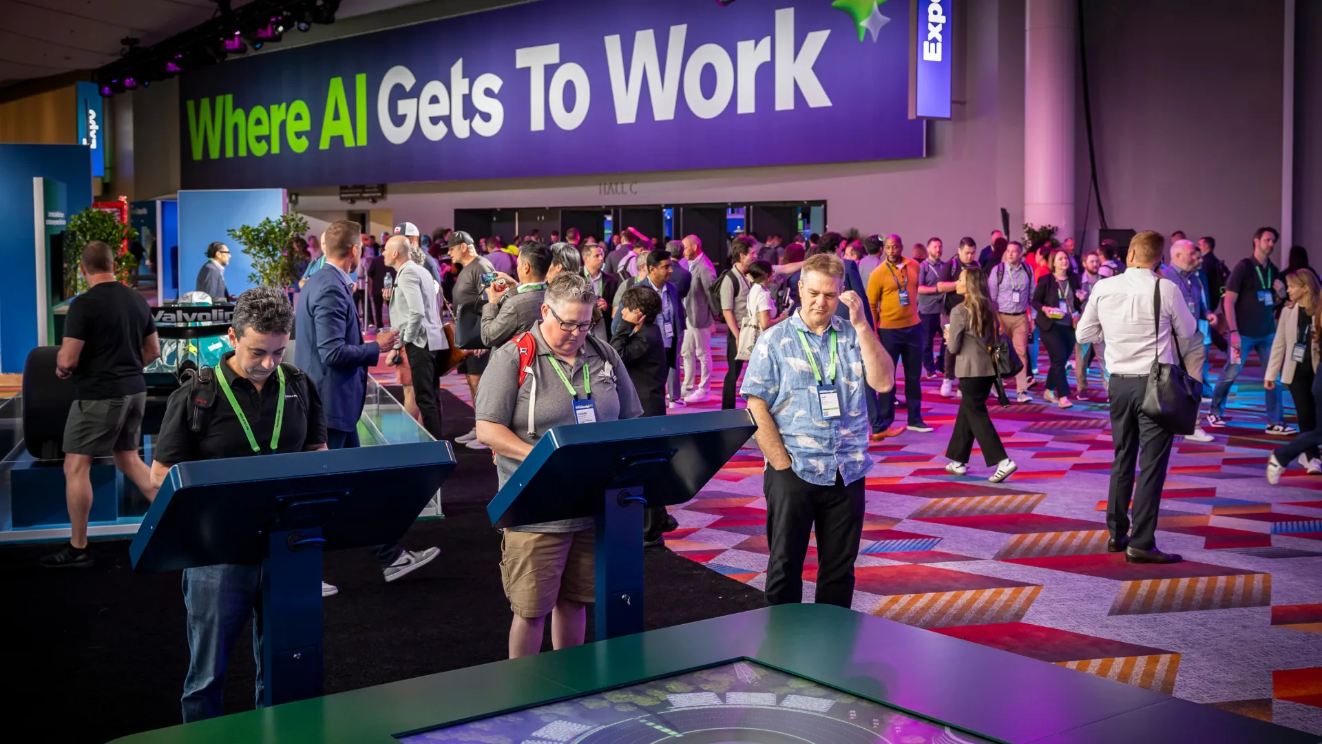 Crowd moves through the Knowledge 2025 expo past staffed touchscreen kiosks