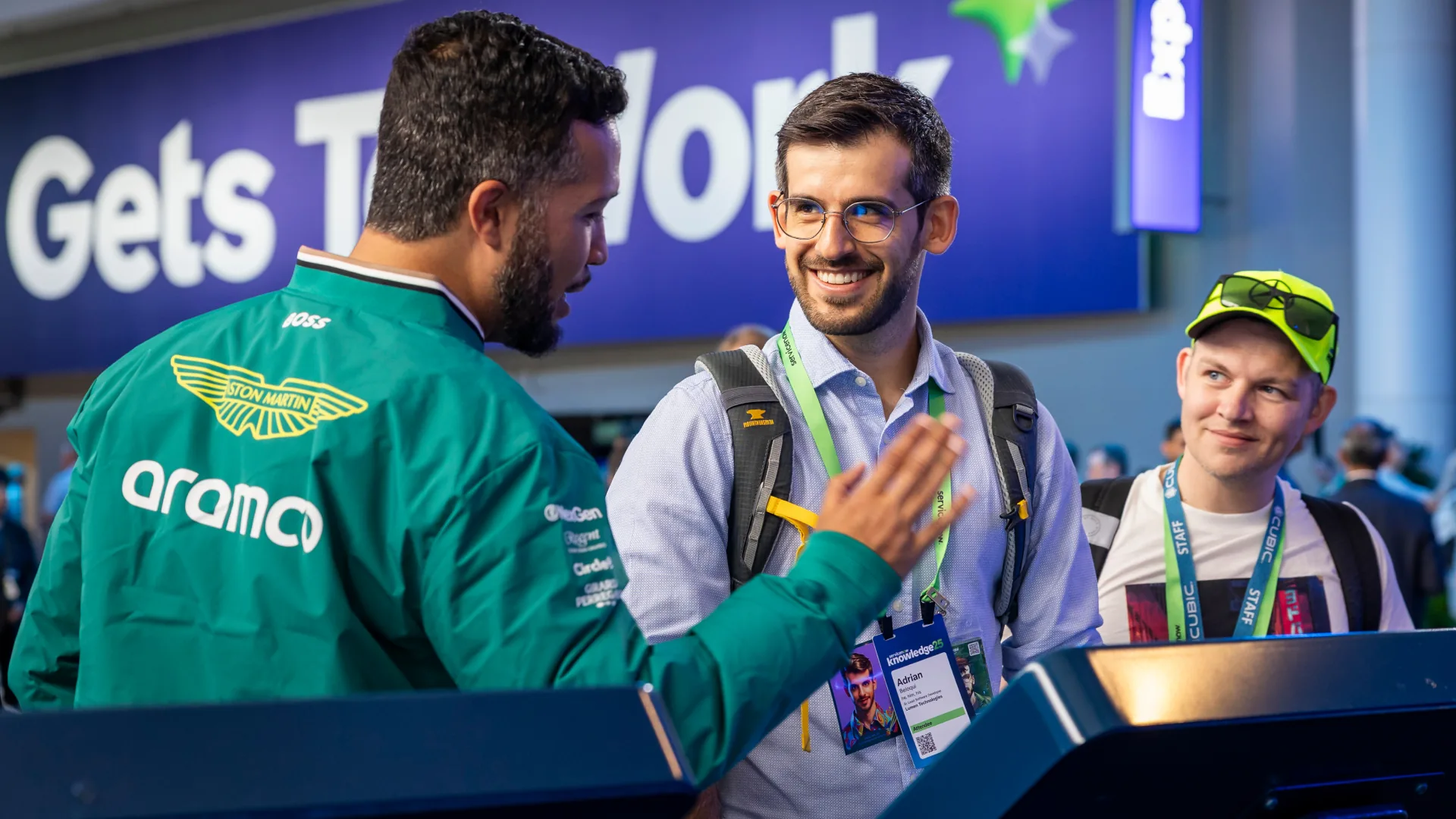 Staffer in an Aston Martin team jacket guides smiling attendees at the F1 activation