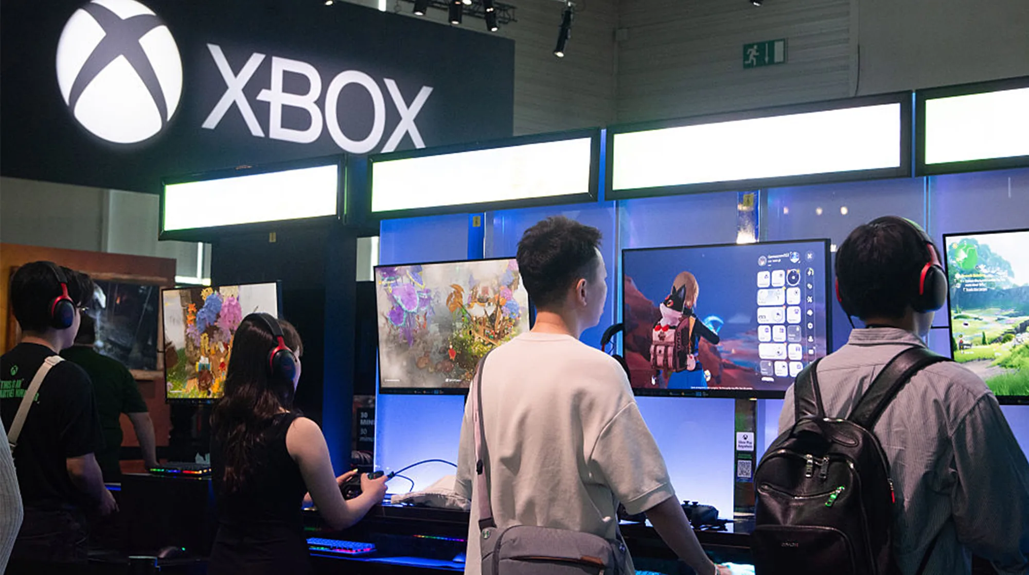 Attendees wearing headsets play games at monitor stations inside an Xbox booth.
